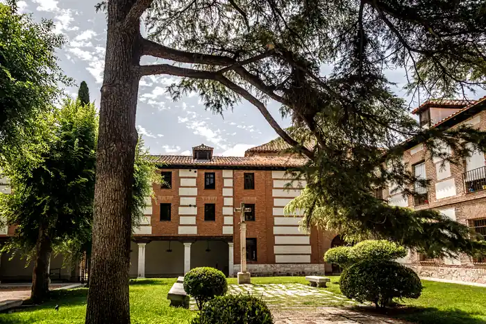 Jardín interior con crucero de piedra y fachada de ladrillo y mampostería del recinto universitario de Alcalá