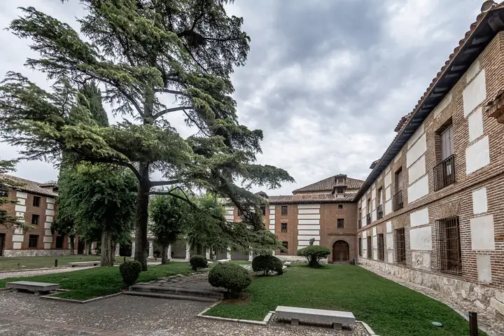 Amplio patio ajardinado con cedros y edificios de ladrillo de la Residencia Universitaria San Ildefonso