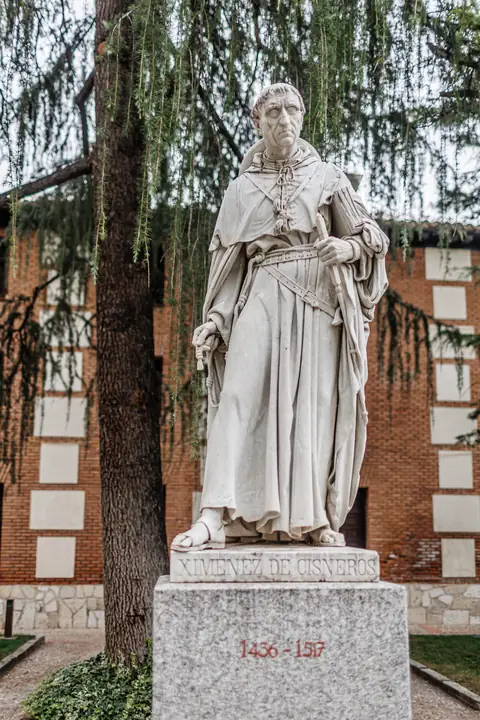 Estatua del cardenal Ximénez de Cisneros (1436-1517) junto a un cedro en un jardín de la residencia
