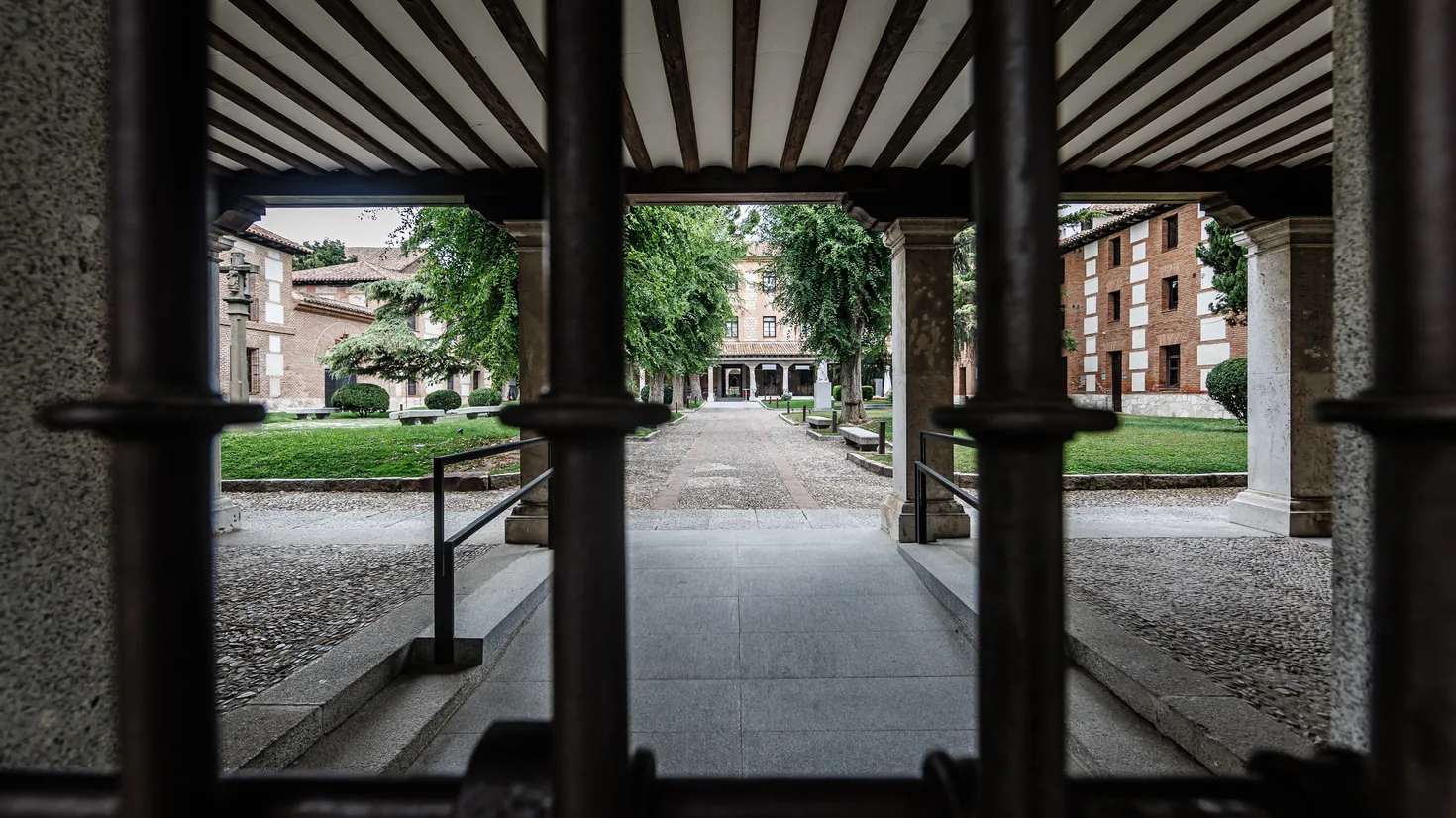Vista desde la galería porticada hacia el patio interior del colegio, con el paseo central empedrado y los edificios de ladrillo al fondo