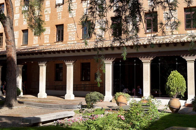Patio ajardinado de la residencia con su porche de columnas y la zona común acristalada al fondo